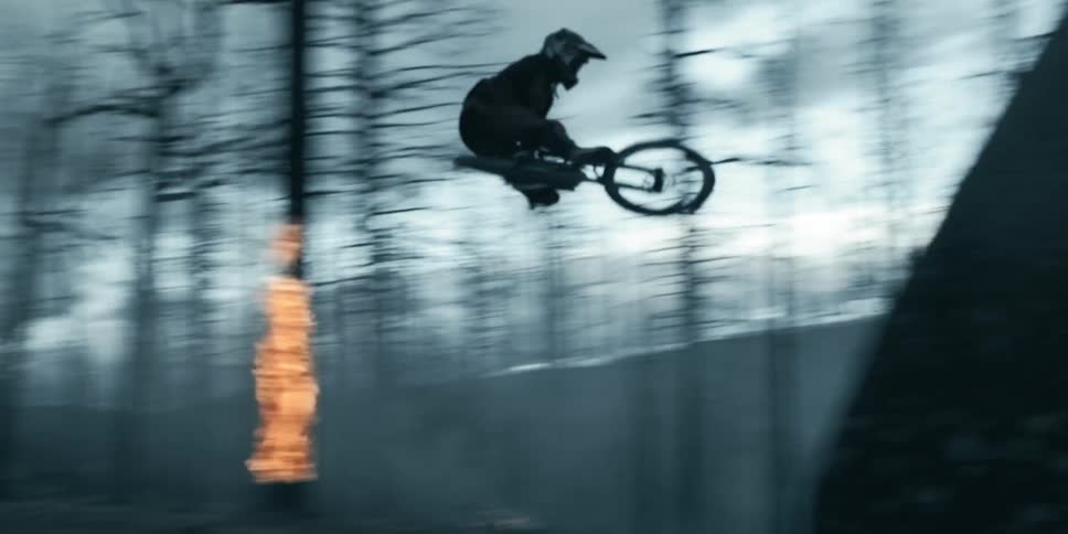 A man rides a mountain bike over a jump in a burning forest