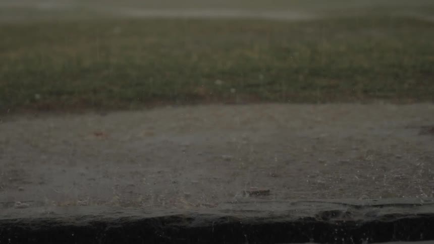 Rain drops falling over a patch of grass and dirt