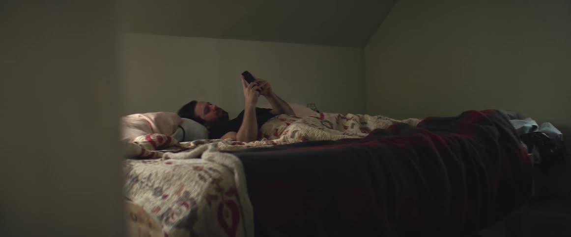 Man laying in bed at home looking at his phone