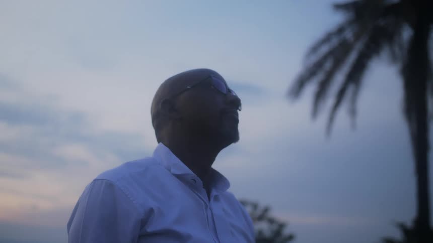 A man is standing outside by a palm tree