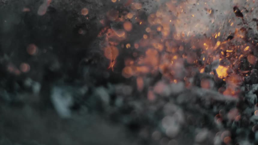 Smoke and embers rise from burning charred wood