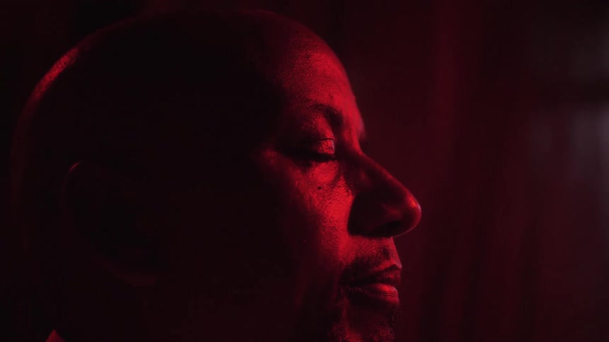 Man with eyes closed standing inside a room under red light