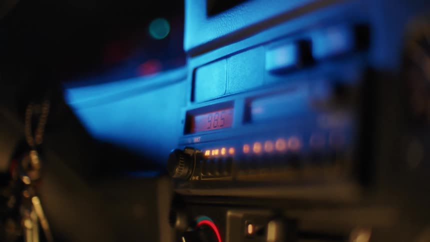 A person driving a car reaches their hand to change the radio station with a button dial at nighttime