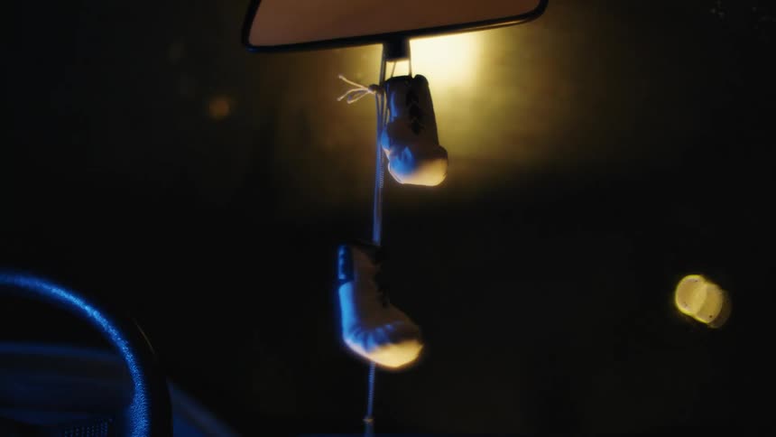 A vehicle with a steering wheel a windshield and a rearview mirror with toy boxing gloves hanged up on it