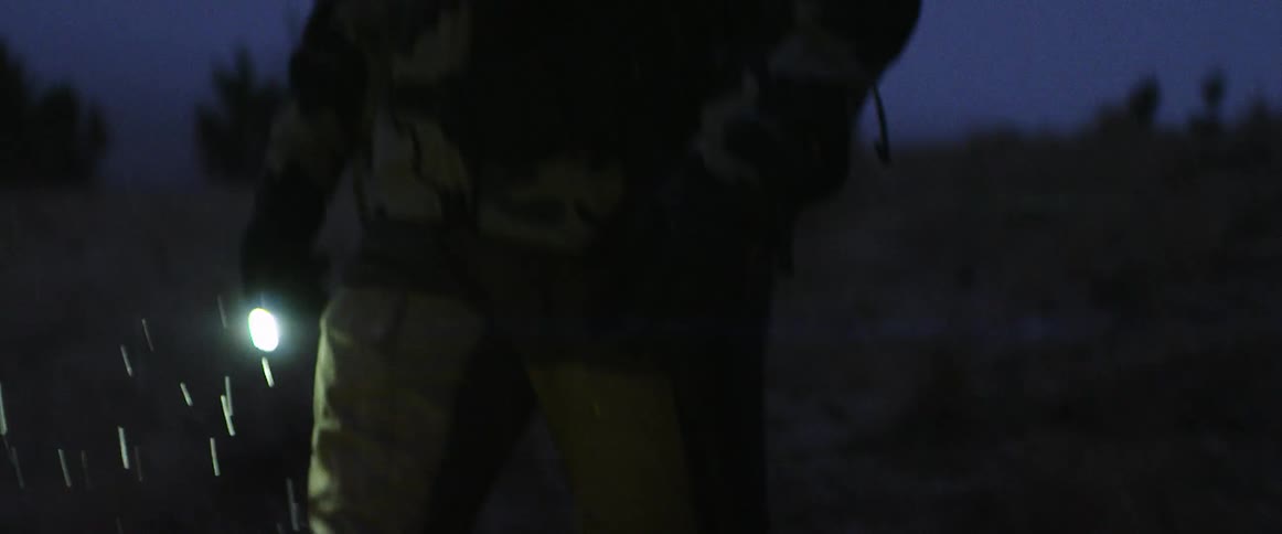 Man walking on a field under the rain with a flashlight at night