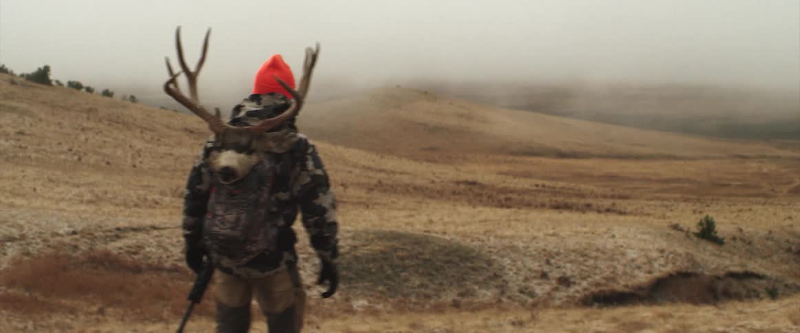 A hunter is walking on the field with antlers on his back
