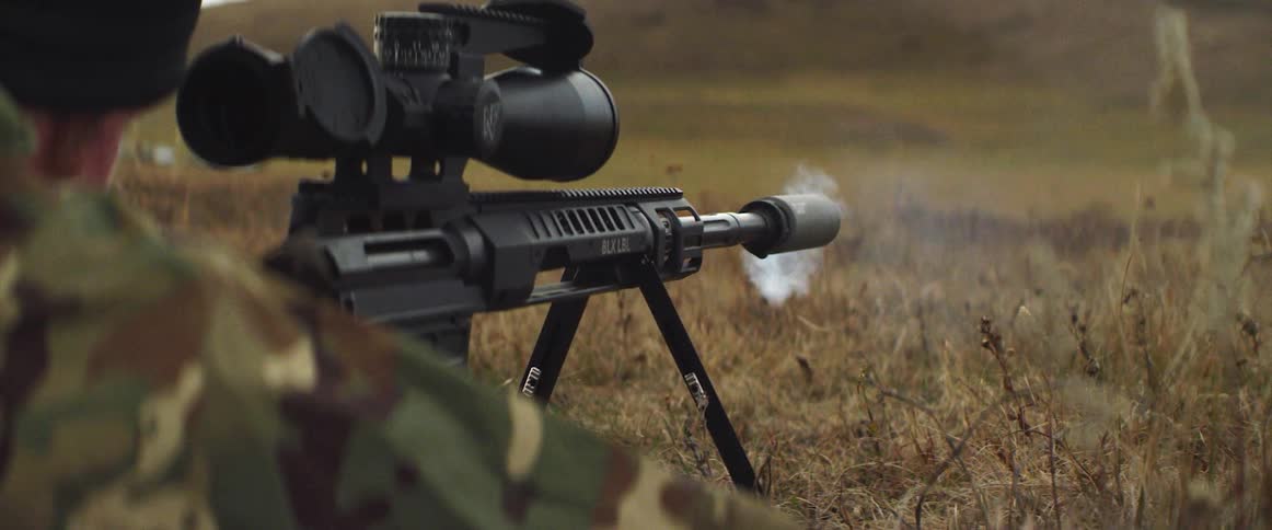 A man with fatigues and a hat shooting a rifle with a scope
