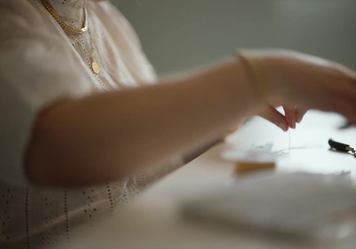 A woman uses thread clippers to cut a thread and wrap the end around a spool while sitting at a table