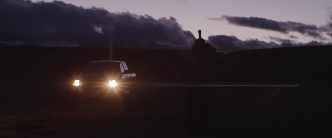 A person runs towards a car carrying a stick