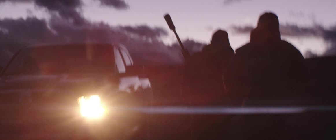 Two soldiers carrying assault rifles walking next to a pickup truck with headlights on at evening