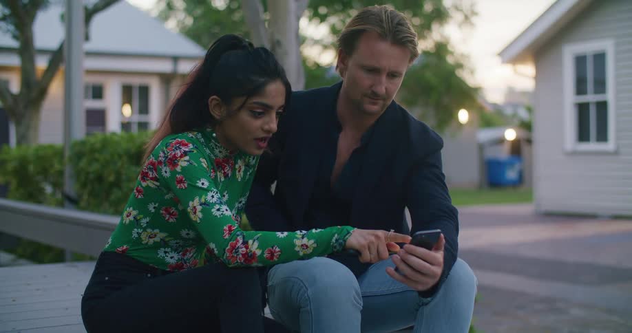 Woman and man sitting on a bench looking at a phone at sunset