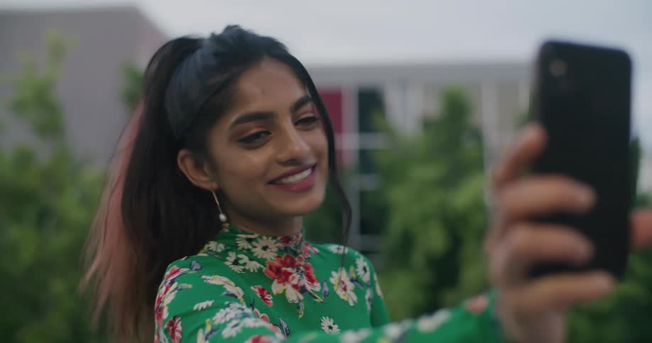 Brunette woman with ponytail and green blouse makes video call on smartphone