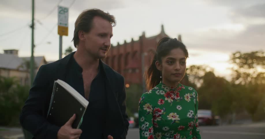 A woman and man walk outside by the road with the man holding a notebook