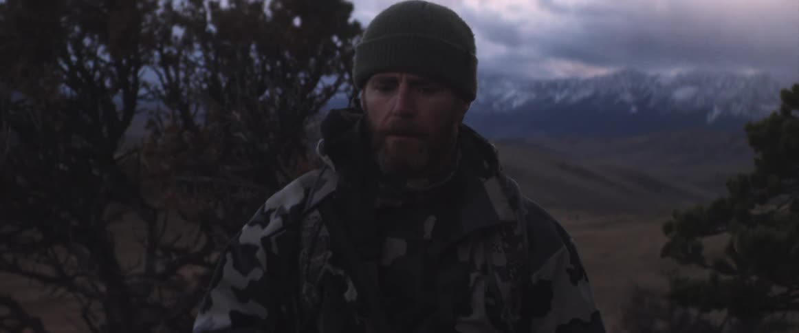 A man hiking up a slope next to a mountain range in the wilderness in the evening