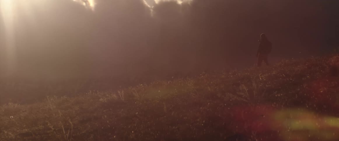Soldier walking on a grass covered hill at sunset