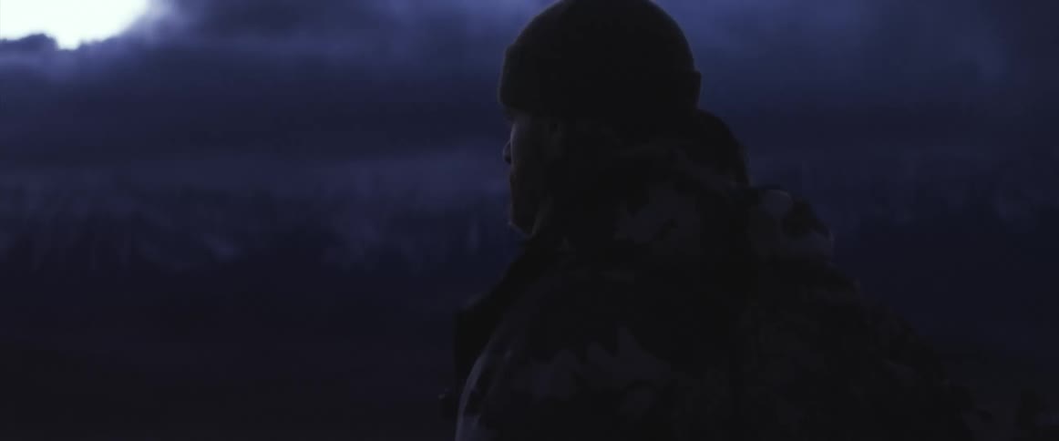 A man standing outdoors in the evening next to a mountain range staring off into the distance
