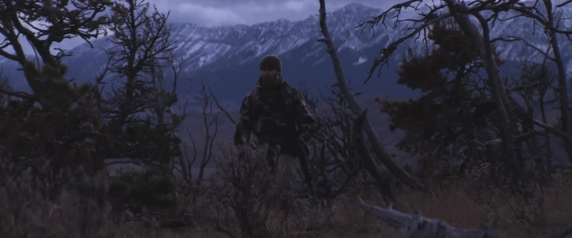 A man walking with a gun in a forest