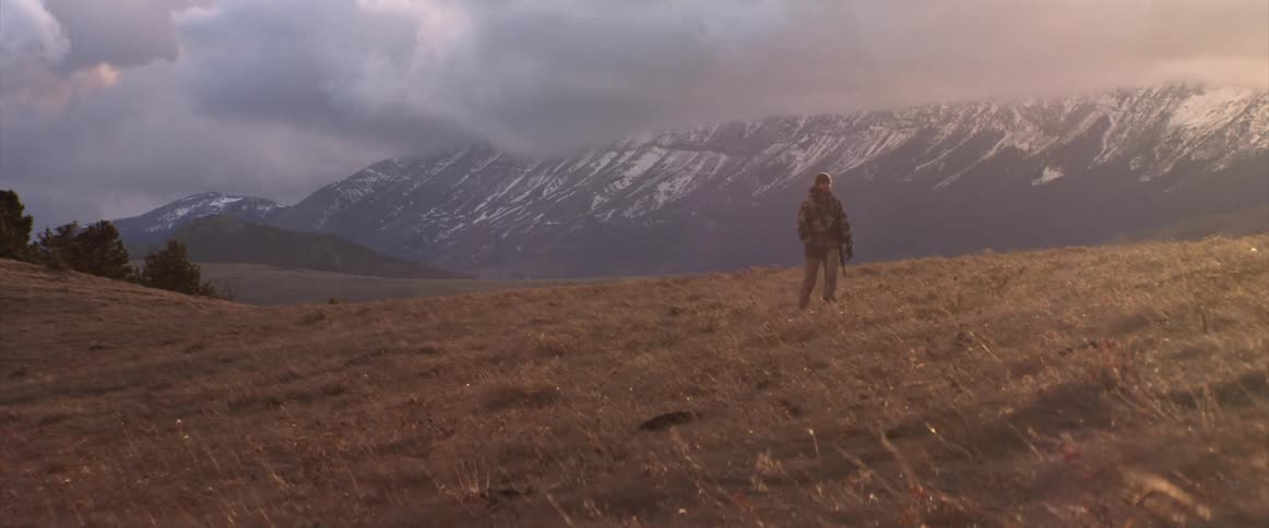 A soldier walking on a hill near the snow covered mountains at sunset