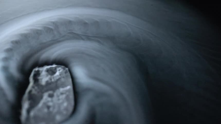 Piece of dry ice spinning on a black surface leaving a swirling trace of white smoke