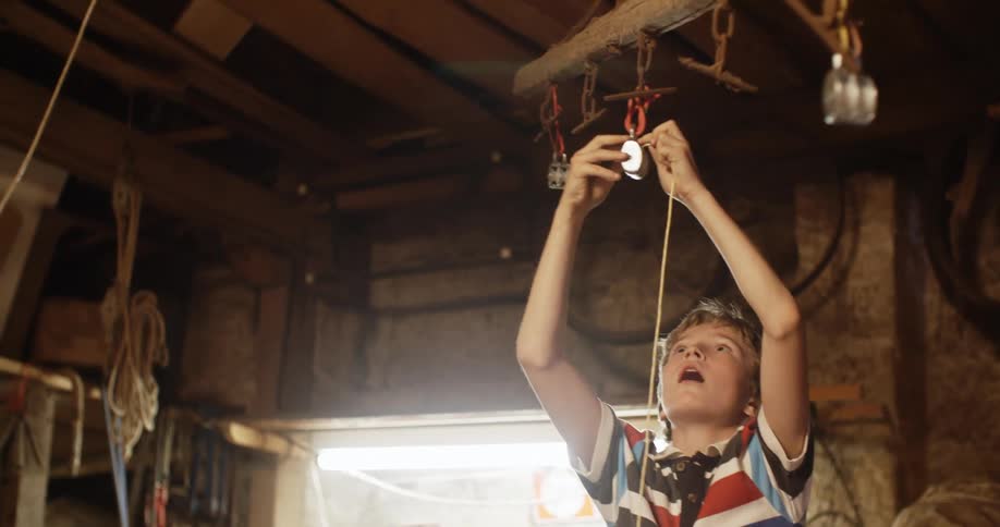 A boy in a workshop putting a string on a pulley with a wall in the background