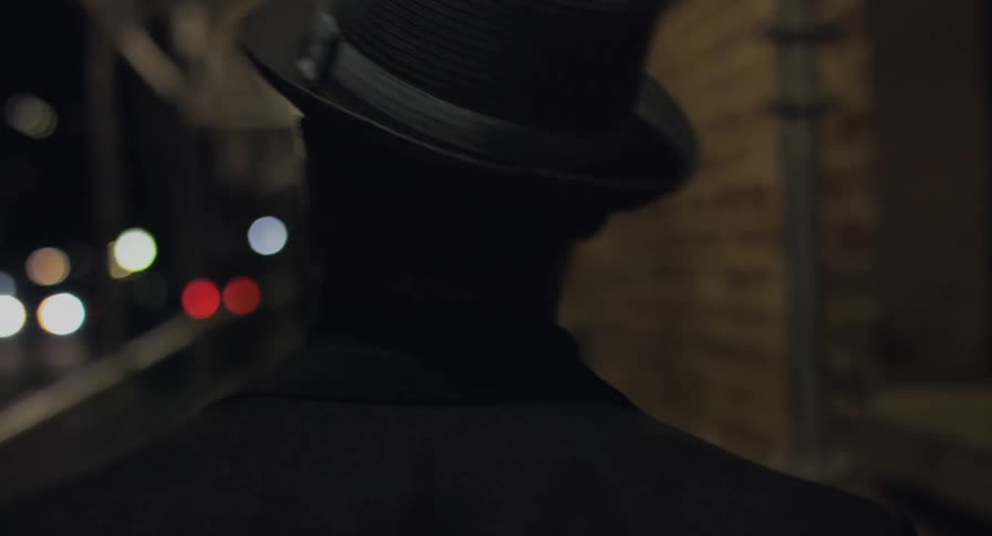 Man wearing a hat walking under the construction scaffolding on the street of a city at night