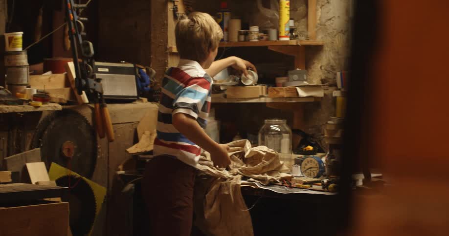 A young boy placing objets on the shelf inside a workshop