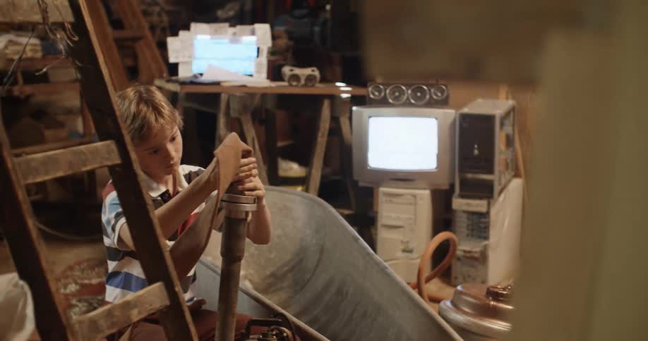 Young blonde boy playing in the basement hooks a hose into a pipe