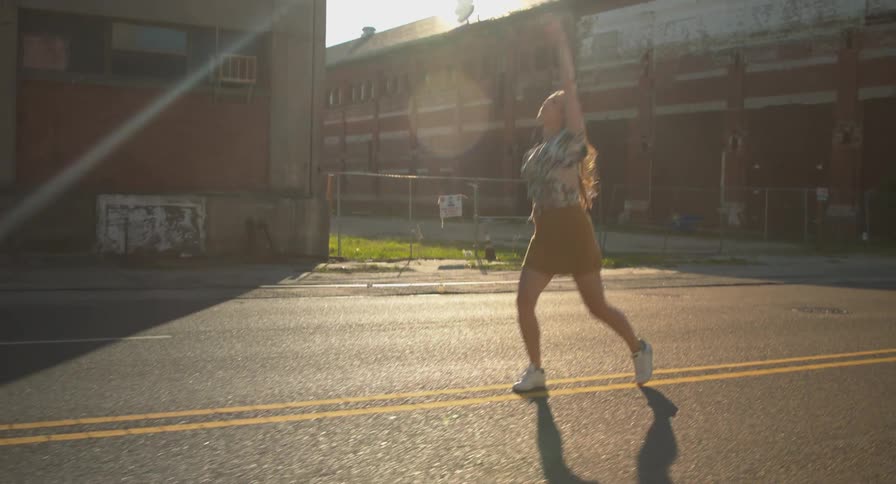 A woman carries her smartphone as she dances down the middle of a deserted street in a city
