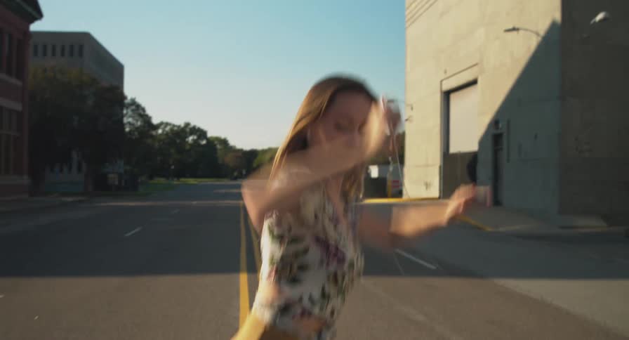 A woman dances in the middle of an empty downtown street with her smartphone in hand