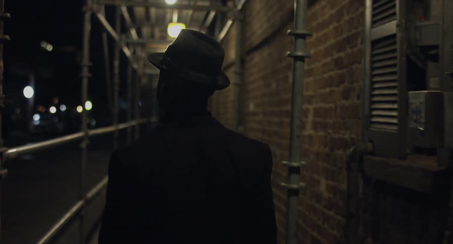A silhouette of a person wearing a hat walking next to a building