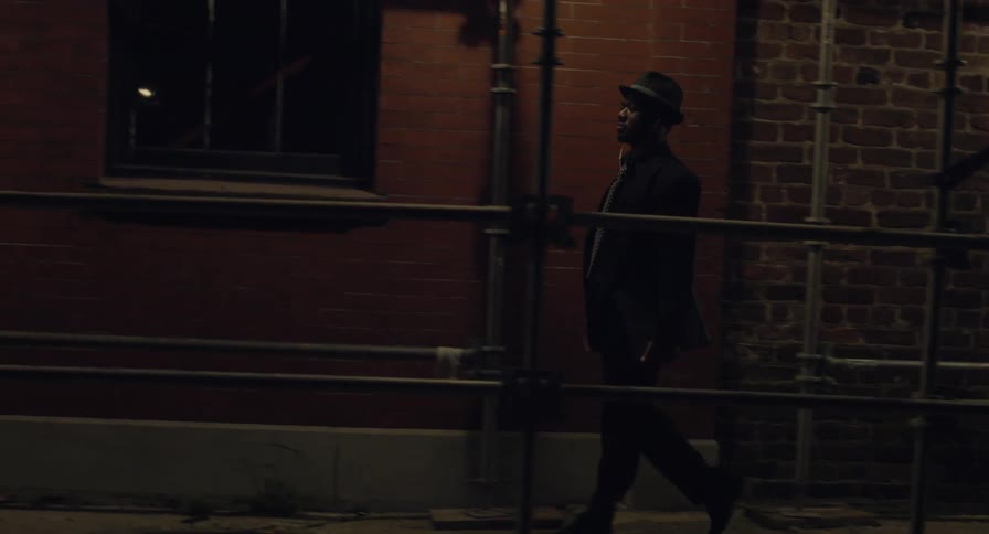 A man wearing a hat walking under the construction on the street of a city at night