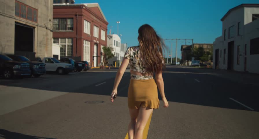 A woman with a smart phone walking and dancing on the street with buildings and the sky in the background