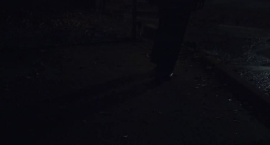 A person walking on a pavement with a puddle of water and lights flashing