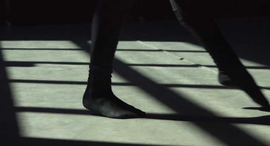 Woman wearing black socks dances acrobatically inside a dimly lit room