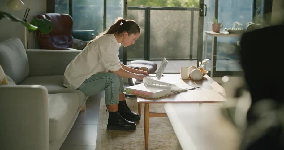 A woman in a room sitting on a couch next to a table typing on a laptop