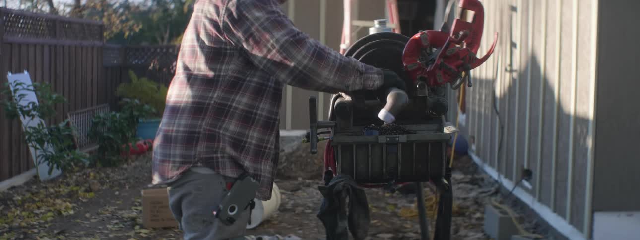 Man runs pipe through machine standing next to building under construction