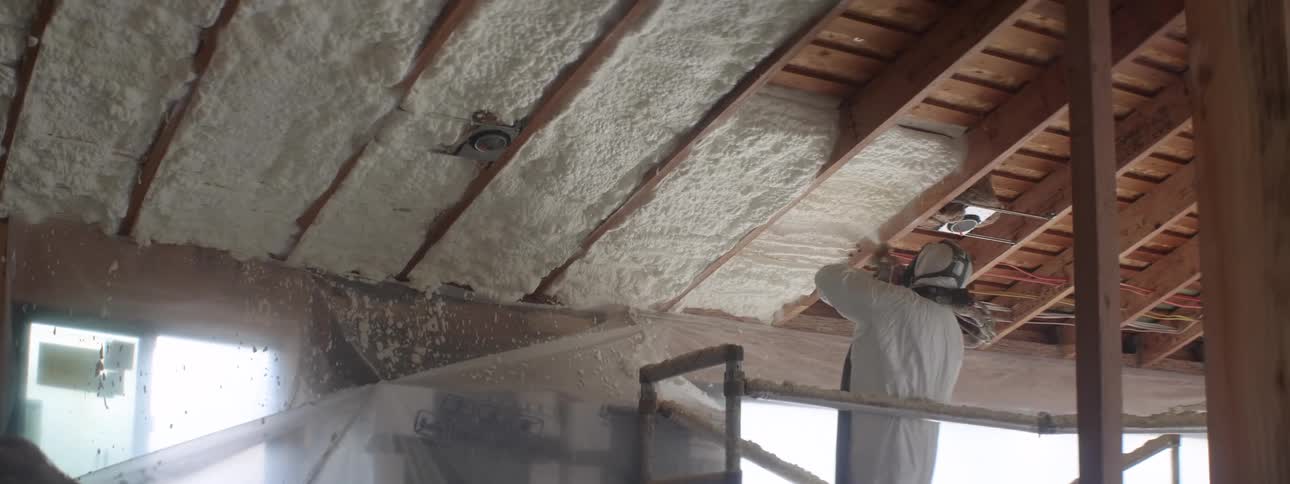 A person with a hazmat suit and a mask spraying insulation on a ceiling