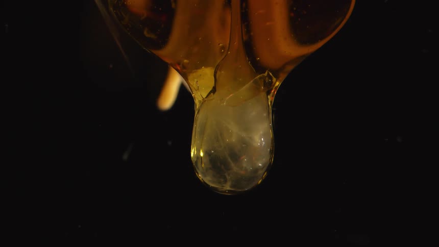 Amber syrup falls into clear liquid leaving tiny floating bubbles