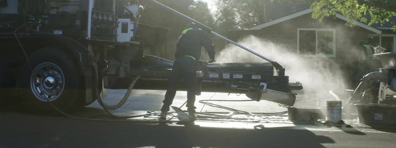 Worker uses a hose to clean machinery outside a construction site