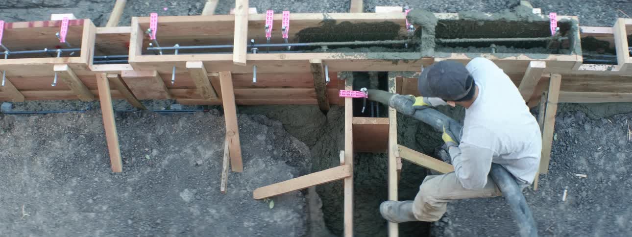 Worker pouring concrete inside a wooden frame outside a house