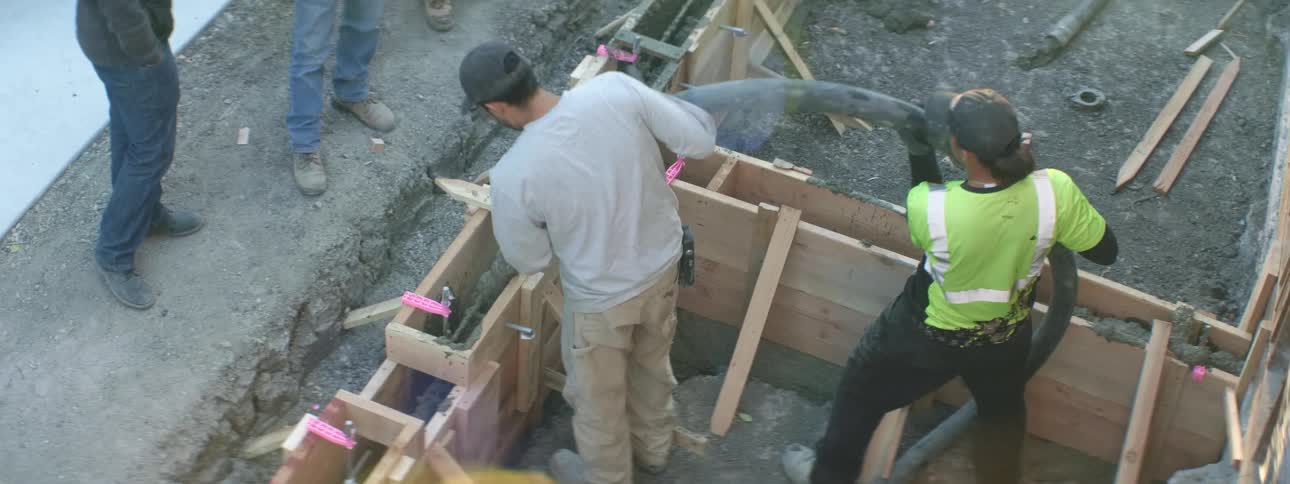 Men with hats pouring cement from a hose