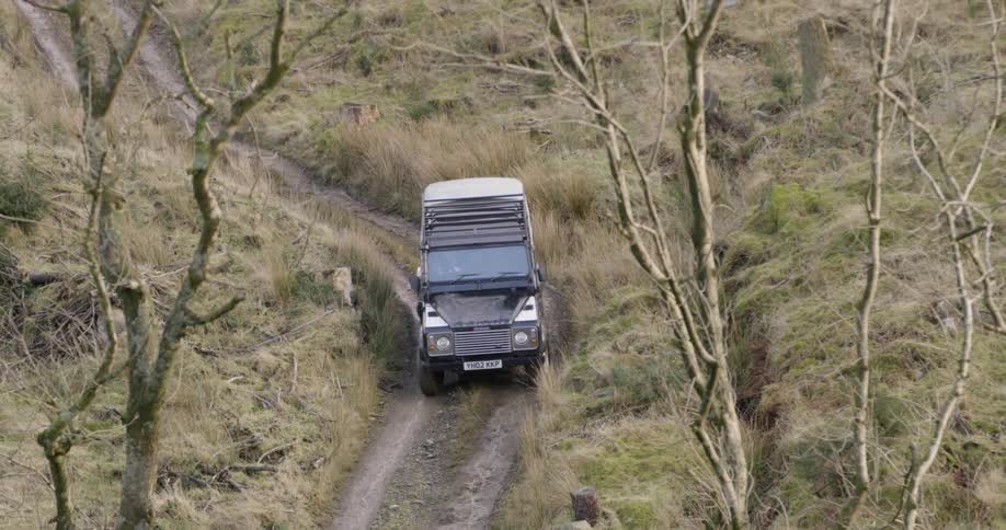 A vehicle driving on a dirt road surrounded by trees and grass