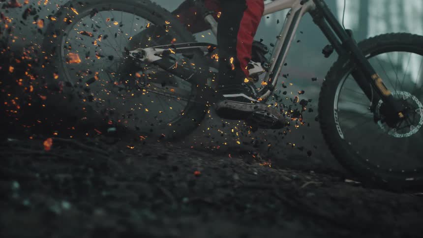 Burning ashes and embers fly into the air as person on a bike rides over them