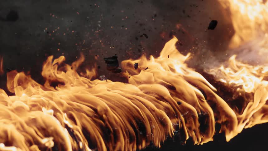 Bike tire rolls over the top of a burning log with flames and embers