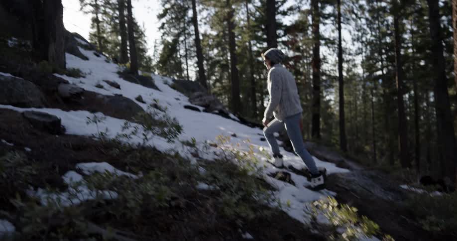 Young woman climbing a slope on the snow covered pine forest at sunset