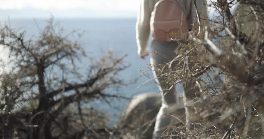 A woman with a backpack and sunglasses hiking by a lake with the sky and clouds in the background