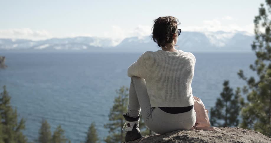 Woman hiking in the mountains sitting on a rock looking at the horizon
