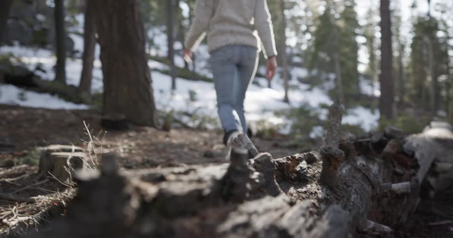 Woman with a woolly hat a grey sweater and jeans walks in the snowy forest