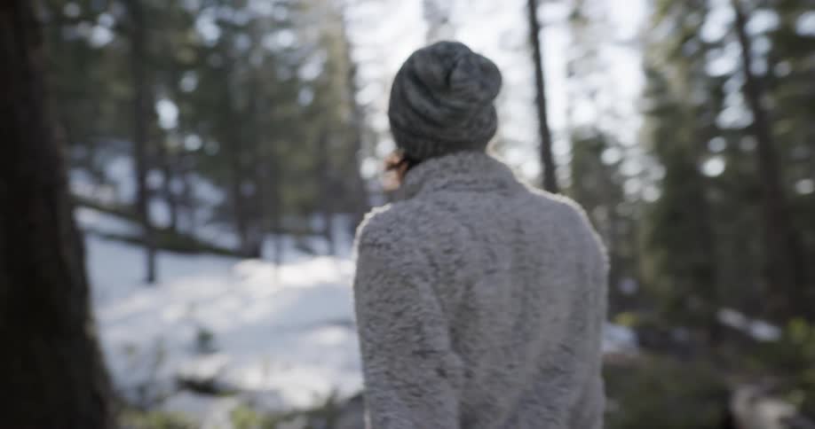 A young woman walks through a snowy woodland during the day