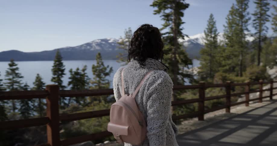 A woman looks at the lake as she walks on a park path on a sunny day